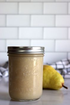 a glass jar filled with liquid sitting on top of a counter next to a pear