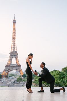 a man kneeling down next to a woman in front of the eiffel tower