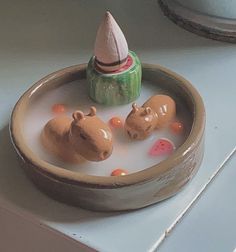 three toy hippos in a bowl of water with a small cone on top