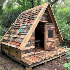 a small wooden cabin in the middle of some trees and grass with a door open