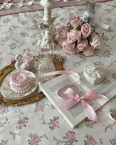 a table topped with lots of pink flowers next to a cake and an open book