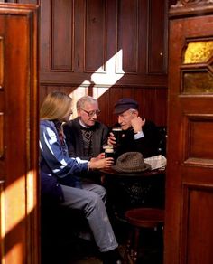 three people sitting at a table in a room with wood paneling and wooden doors