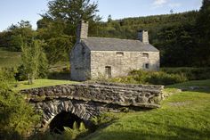 an old stone house in the middle of a field with trees and bushes around it