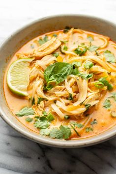 a white bowl filled with noodles and garnished with cilantro, parsley and lime