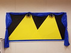 a bulletin board with two yellow and black triangles on it's sides, hanging from the wall