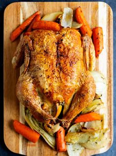 a roasted chicken with carrots and onions on a cutting board