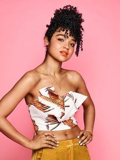 a young woman posing in front of a pink background wearing a white and orange top