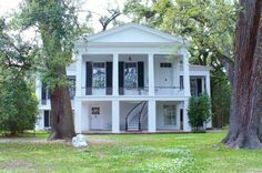 a large white house surrounded by trees in the middle of a park with stairs leading up to it's second story