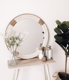 a round mirror sitting on top of a wooden table next to a potted plant