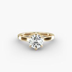 a yellow gold engagement ring with a round brilliant cut diamond in the center, on a white background