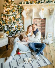 a man and woman sitting on the floor in front of a christmas tree