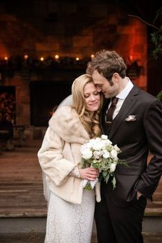 a bride and groom standing together in front of a fireplace