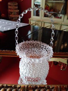 a clear glass vase sitting on top of a wooden table next to a mirror with beads hanging from it