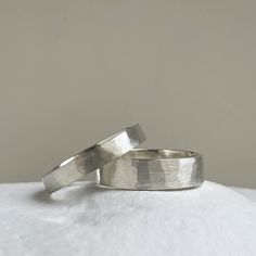 two silver rings sitting on top of a white cloth covered surface, one is made out of metal and the other has a thin band