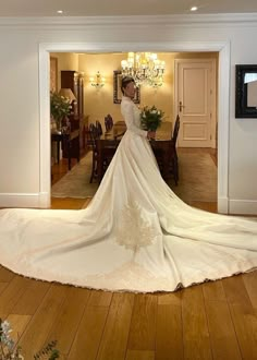 a woman in a white wedding dress is standing near a chandelier and dining room table