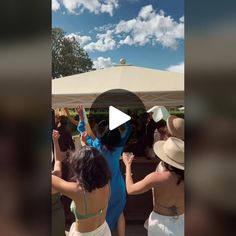 several women dancing under an umbrella at a party in white dresses and straw hats with their arms raised