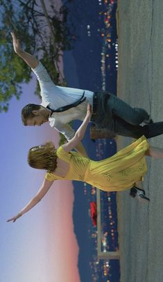 a man and woman are dancing in the street at night with city lights behind them