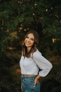 a woman standing in front of a tree smiling at the camera with her hands on her hips