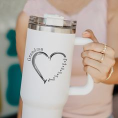 a woman holding a white coffee cup with a heart on the side and grandma written on it