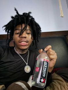 a young man with dreadlocks holding a bottle of energy drink in his hand