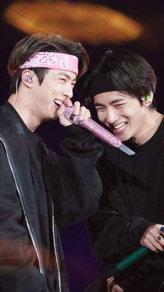 two young men with headbands on singing into microphones and smiling at each other