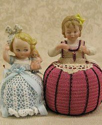 two figurines sitting next to each other on top of a cloth covered surface