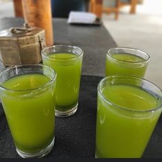 three glasses filled with green liquid sitting on top of a black table next to each other