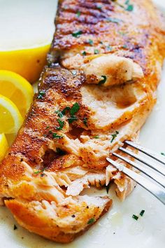 a piece of fish on a plate with lemons and parsley