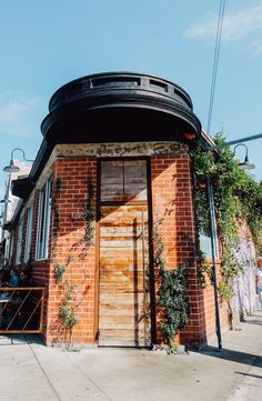 an old brick building with plants growing on it's side and people sitting at the door