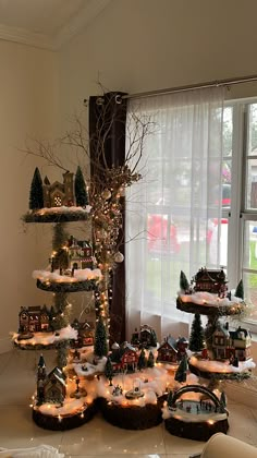 a christmas tree is decorated with miniature houses and trees in front of a large window