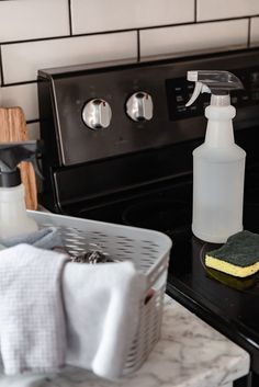 a black stove top oven sitting next to a white basket filled with cleaning supplies and a spray bottle