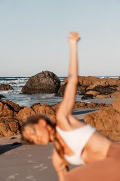 a woman doing yoga on the beach with her arms in the air and one hand up