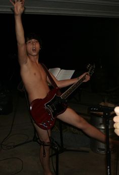 a shirtless man holding a guitar in his right hand