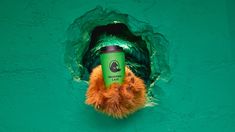 a stuffed animal holding onto a green cup in the middle of a hole on a wall