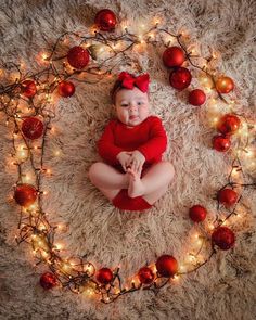 a baby in a red outfit sitting on a rug surrounded by christmas lights