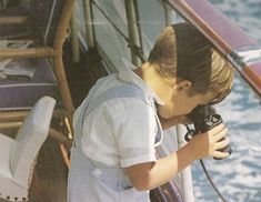 a young boy holding a camera on top of a boat