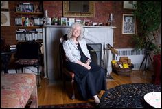 an older woman sitting on a chair in front of a fireplace