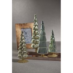 three small christmas trees on a table next to a mirror and wooden frame with a framed photo in the background