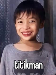 a young boy smiling and wearing a batman t - shirt with the words tikiman on it