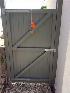 an orange flower hanging on the side of a wooden gate with gravel in front of it