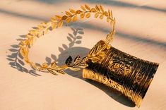 a gold and black vase sitting on top of a white table next to a leafy plant