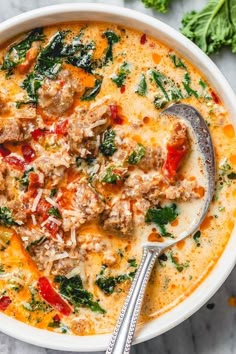 a bowl of soup with meat and spinach on the side next to a spoon