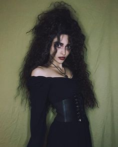 a woman with long hair and black makeup wearing a corset is standing in front of a green wall