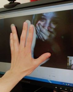 a person's hand reaching up towards a television screen with the image of a woman on it