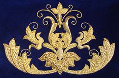 an ornate gold brooch with leaves and scrolls on a dark blue velvet background,