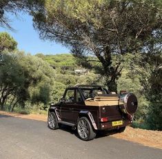 a brown jeep parked on the side of a road next to some green trees and bushes