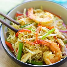 a bowl filled with shrimp and veggies next to chopsticks on a table