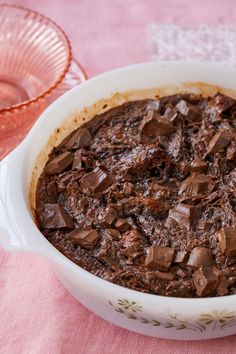 a chocolate cake in a white dish on a pink table cloth next to a glass bowl