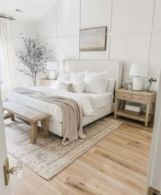 a white bedroom with wood floors and a large bed in the center, along with two nightstands on either side of the bed