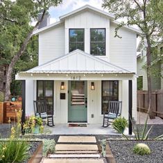 two rocking chairs are sitting in front of the door to a small white house with green shutters